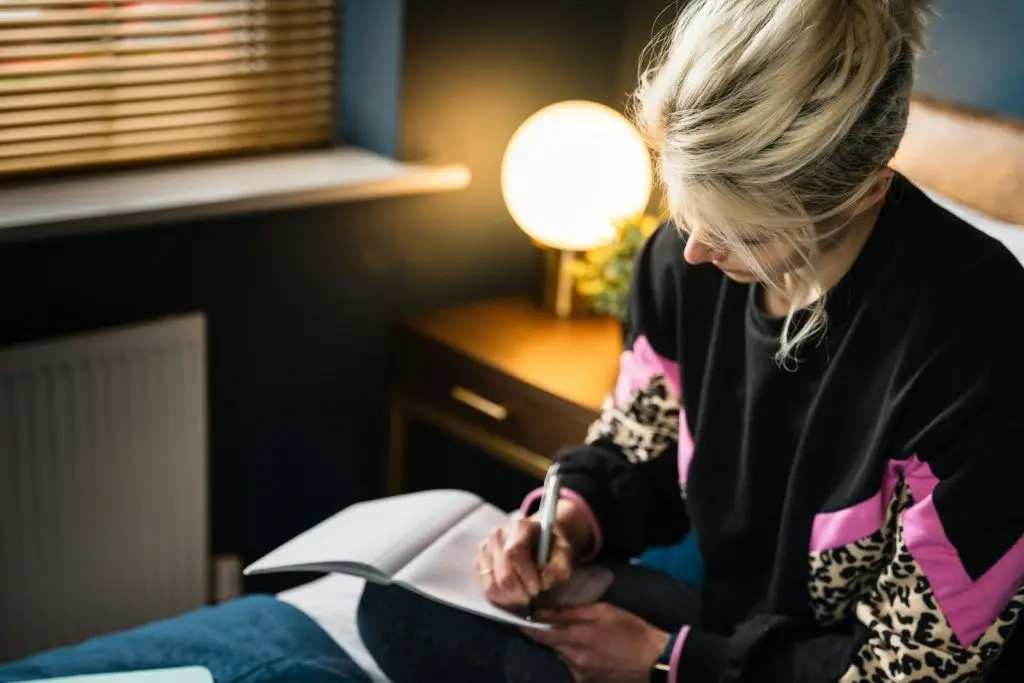 woman in black and white long sleeve shirt sitting on bed and working through some shadow work journaling prompts
