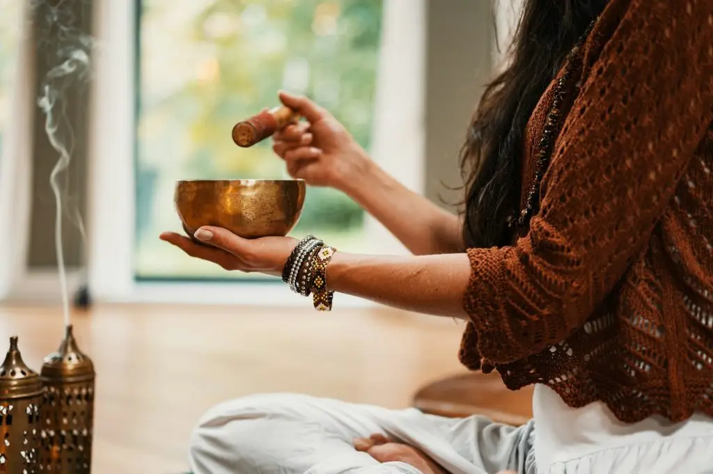 woman in brown knit sweater holding a metal singing bowl