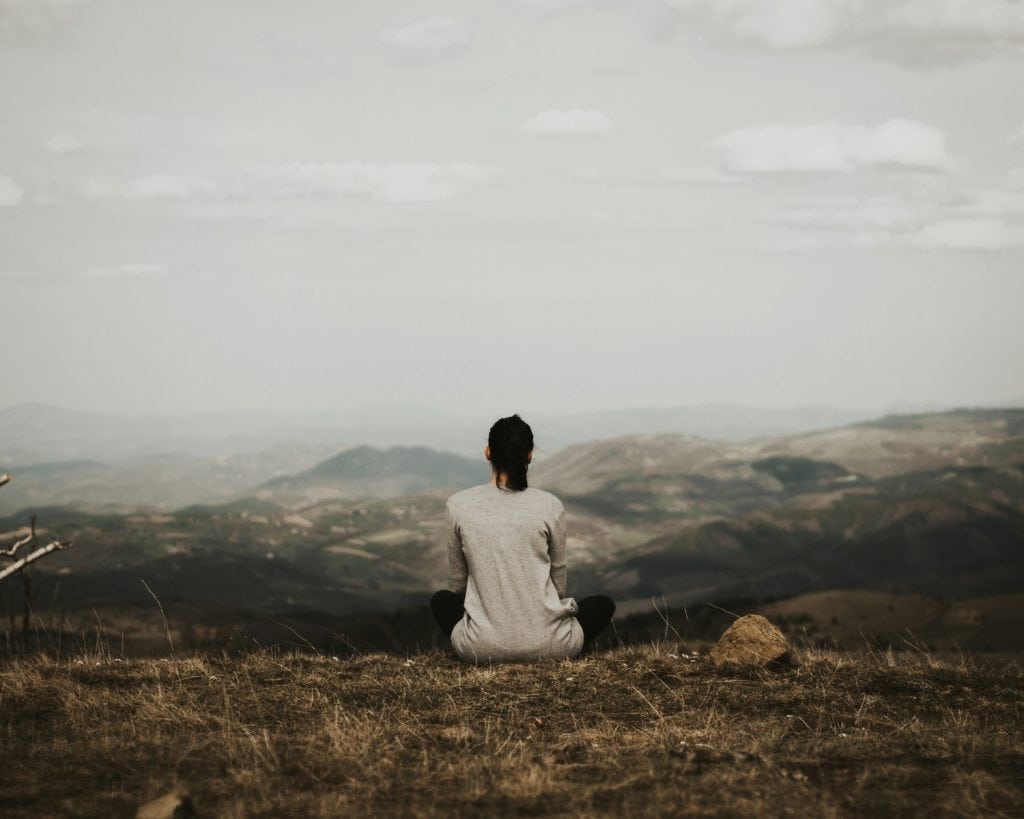 woman sitting on cliff overlooking mountains during daytime integrating her Lions Gate portal downloads