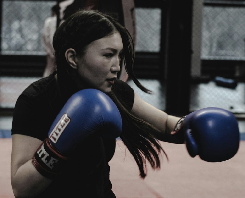 A woman in a black shirt and blue boxing gloves representing standing in the energy of the Hunter Moon in Aries
