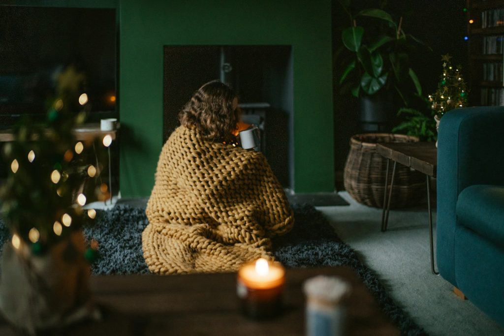 a woman wrapped in a blanket sitting on a rug in a living room enjoying the autumn equinox spiritual lessons