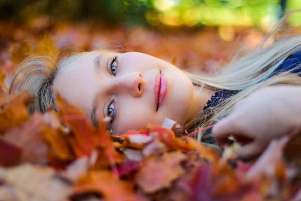 woman wearing blue top lying on dried maple leaves during daytime photography - connecting to October's spiritual energy